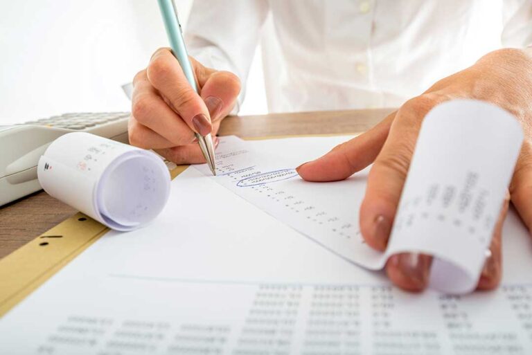 A couple reviews documents at their kitchen table with a calculator, surrounded by receipts and tax forms.