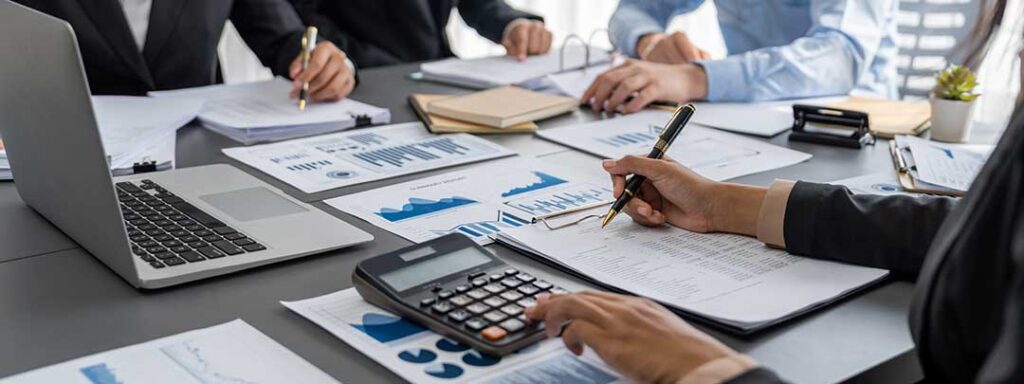 A couple reviews tax forms and household financial records with a calculator at a kitchen table.